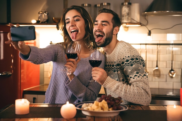 Beau jeune couple heureux, passer une soirée romantique ensemble à la maison, boire du vin rouge, prendre un selfie