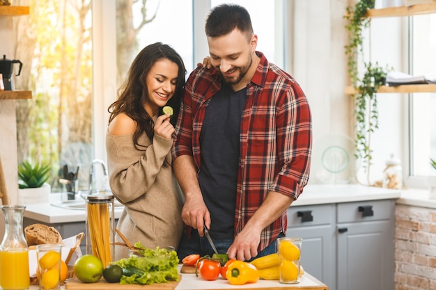 Beau jeune couple heureux souriant parle et souriant tout en cuisinant des aliments sains dans la cuisine à la maison.