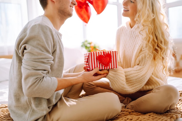 Beau jeune couple à la maison célébrant la Saint-Valentin Les amoureux se donnent des cadeaux