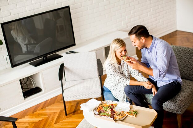 Beau jeune couple manger des pizzas dans la chambre