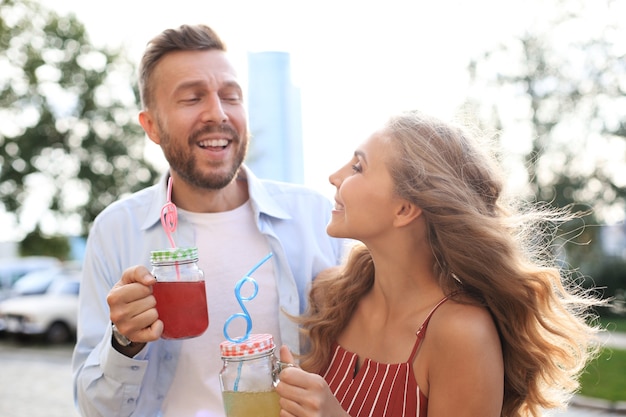 Beau jeune couple marchant dans la rue de la ville, souriant et buvant des cocktails frais.