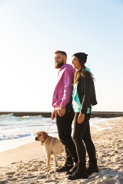 Beau jeune couple marchant avec leur chien à la plage