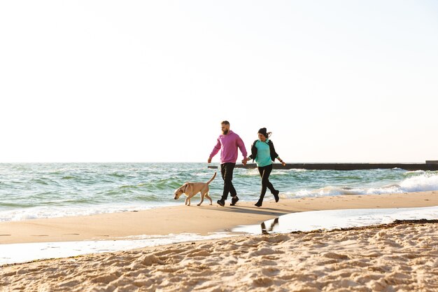 Beau jeune couple marchant avec leur chien à la plage