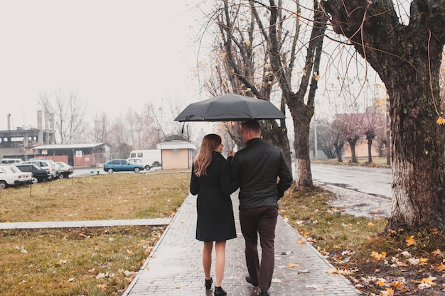 Beau jeune couple marchant sous un parapluie dans l'allée d'automne