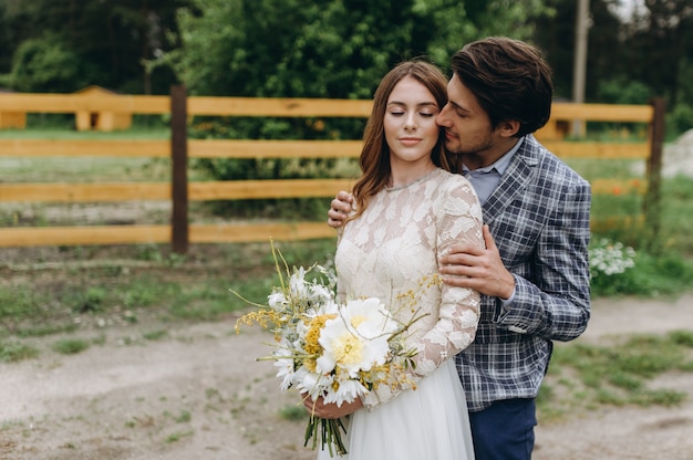 Beau jeune couple mariée et le marié marchant près de la clôture en bois