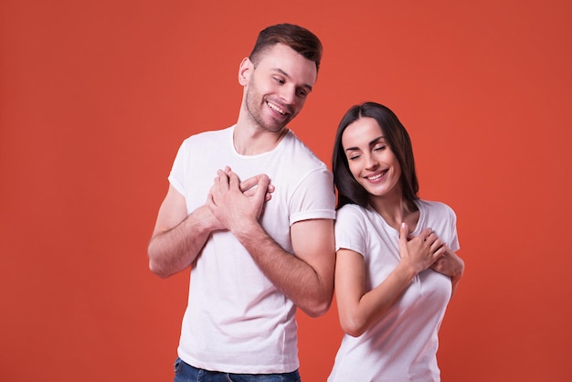 Beau jeune couple mignon amoureux en t-shirts blancs leur tenant les mains sur la poitrine. Couple amoureux. La saint Valentin