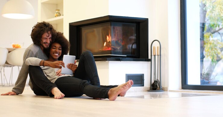 Photo beau jeune couple multiethnique utilisant un ordinateur tablette sur le sol de leur maison de luxe devant la cheminée le jour de l'automne