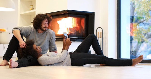 beau jeune couple multiethnique utilisant un ordinateur tablette sur le sol de leur maison de luxe devant la cheminée le jour de l'automne