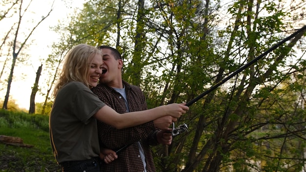 Beau jeune couple pêchant ensemble au bord d'une rivière du lac tromper et sourire coup de côté