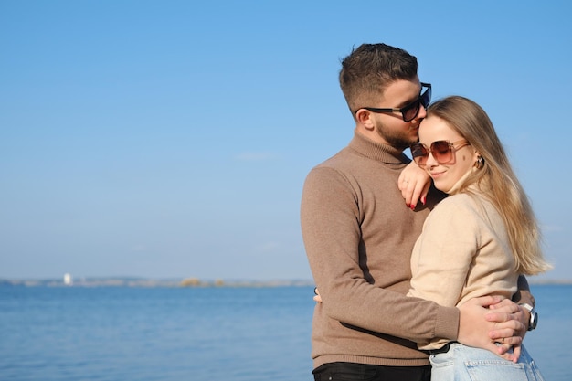 Beau jeune couple posant contre le ciel bleu et l'eau Le gars embrasse la fille et l'embrasse