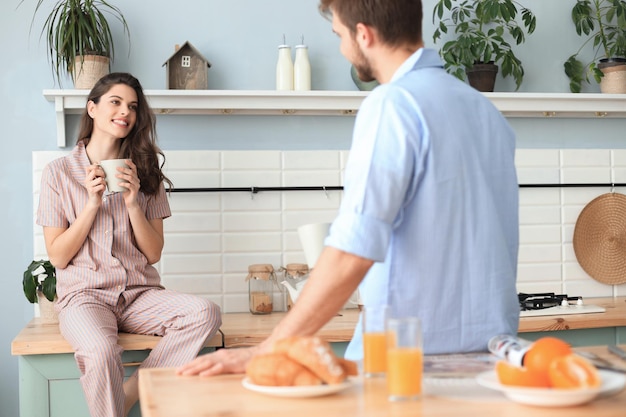 Un beau jeune couple en pyjama se regarde et sourit en cuisinant dans la cuisine à la maison.