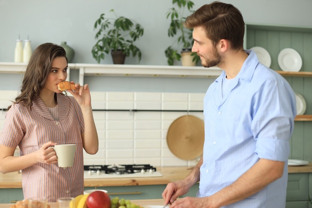 Beau jeune couple en pyjama se regarde et sourit en cuisinant dans la cuisine à la maison.