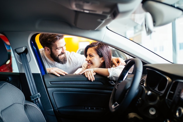 Beau jeune couple à la salle d'exposition de voitures choisissant une nouvelle voiture à acheter.