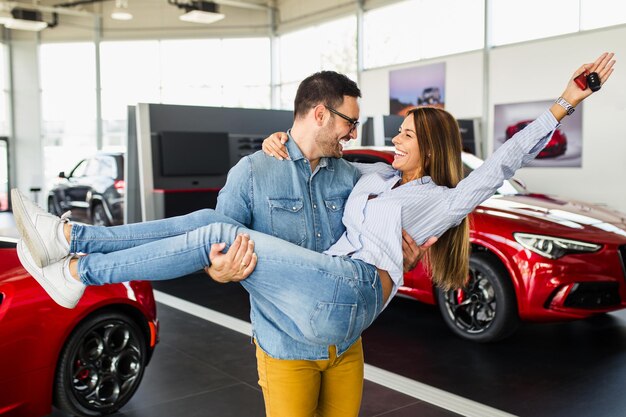 Beau jeune couple à la salle d'exposition de voitures est sorti en raison de l'achat d'une nouvelle voiture.