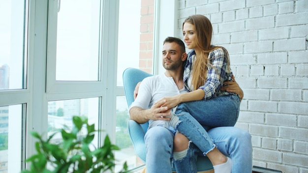 Beau jeune couple se détendre assis sur une chaise et profiter de la vue depuis le balcon du nouvel appartement loft