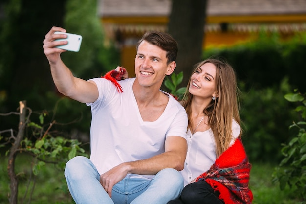 Beau jeune couple se détendre dans le parc et fait selfie