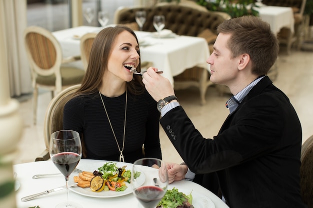 Beau jeune couple se nourrissant et souriant tout en passant du temps au restaurant