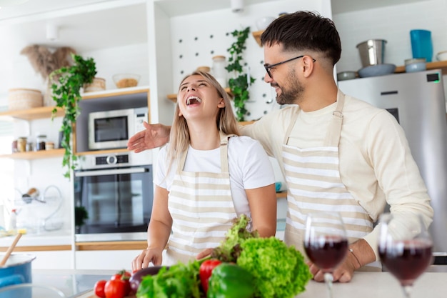 Un beau jeune couple se nourrit l'un l'autre et sourit tout en cuisinant dans la cuisine à la maison Un couple sportif heureux prépare de la nourriture saine sur une cuisine légère Concept de nourriture saine