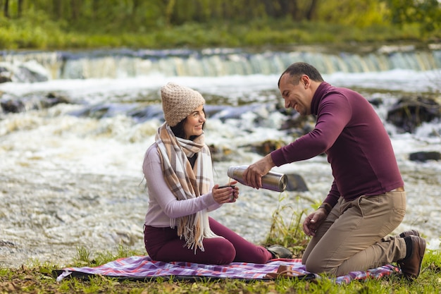 Un beau jeune couple se repose sur les rives d'une rivière d'automne