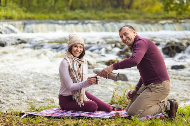 Un beau jeune couple se repose sur les rives d'une rivière d'automne