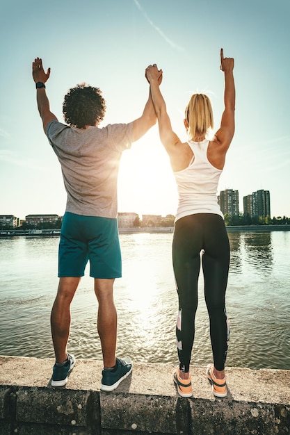 Un beau jeune couple se tient sur un mur au bord de la rivière et salue le soleil après l'entraînement.