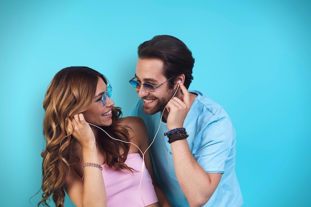 Beau jeune couple souriant au casque écoutant de la musique en se tenant debout sur fond bleu