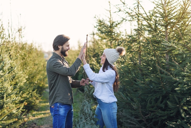 Beau jeune couple souriant élégant se lie avec des fils bel arbre de Noël et donnant cinq hauts.