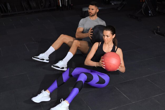 Un beau jeune couple sportif s'entraîne avec un ballon de médecine dans la salle de sport.