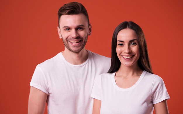 Beau jeune couple en t-shirts blancs vierges posent sur fond orange. Relation, famille, publicité