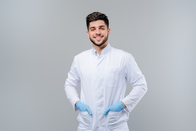 Beau jeune docteur en gants isolé sur gris