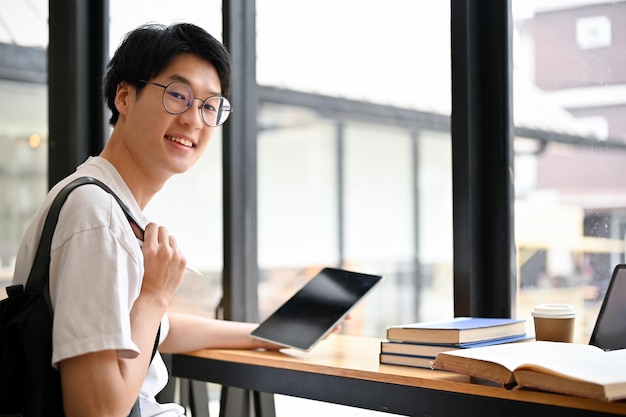 Beau jeune étudiant asiatique portant des lunettes est assis à une table dans un café