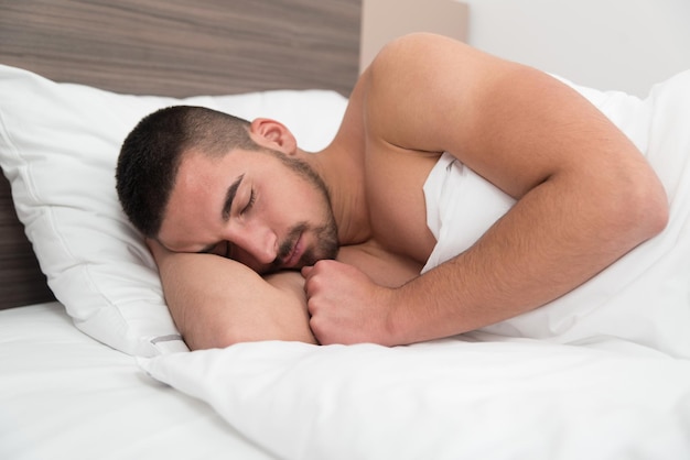 Beau jeune étudiant masculin heureusement dormir dans un lit blanc