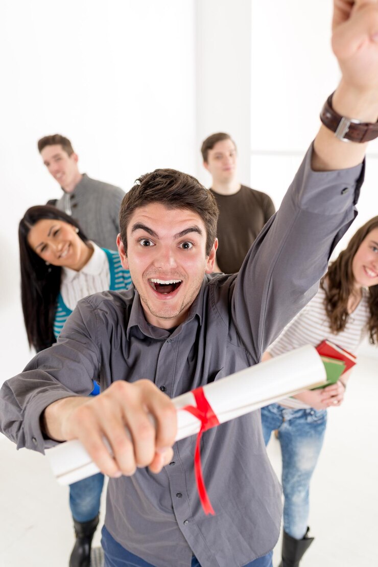 Un beau jeune étudiant souriant avec diplôme se tient au premier plan. Un groupe heureux de ses amis est derrière lui avec les bras levés dans un poing en l'air.Regardant la caméra