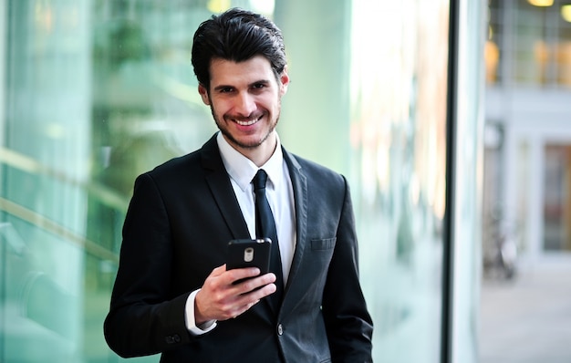 Beau jeune gestionnaire à l'aide d'un smartphone en plein air