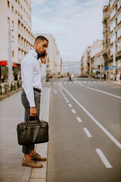 Beau jeune homme d'affaires afro-américain à l'aide d'un téléphone mobile en attendant un taxi en attendant un taxi dans la rue