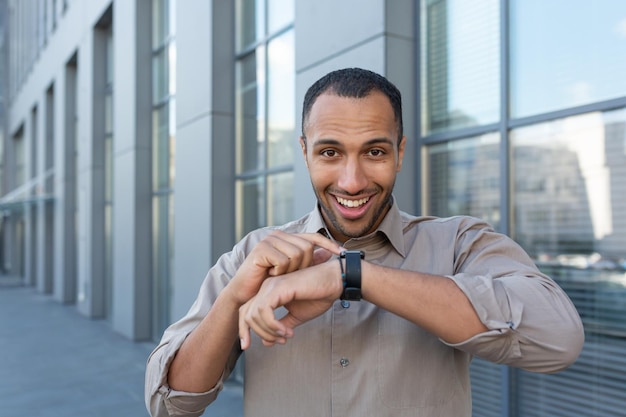 Beau jeune homme d'affaires afro-américain hispanique parlant sur une montre intelligente, il se tient dans la rue