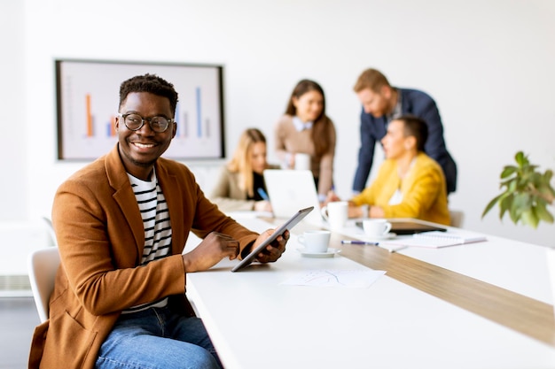 Beau jeune homme d'affaires afro-américain travaillant avec une tablette numérique devant ses collègues à la salle de conférence