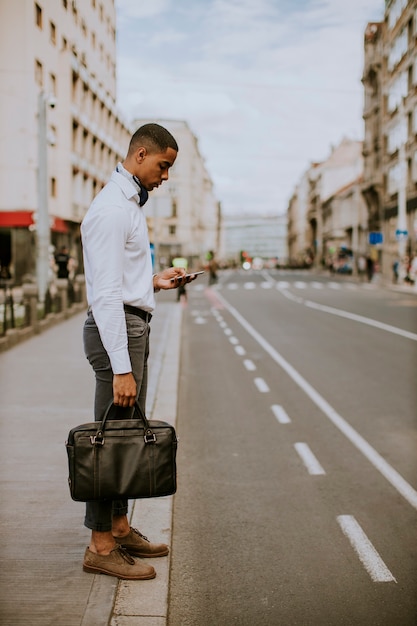 Beau jeune homme d'affaires à l'aide d'un téléphone mobile en attendant un taxi en attente d'un taxi dans une rue