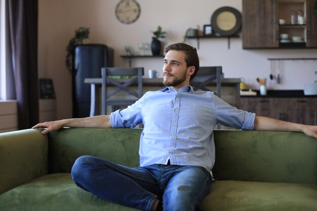 Beau jeune homme d'affaires a l'air détendu tout en étant assis sur le canapé à la maison.