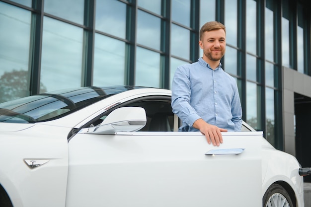 Beau jeune homme d'affaires debout près de sa voiture à l'extérieur