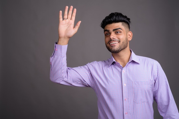 Beau jeune homme d'affaires indien contre le mur gris