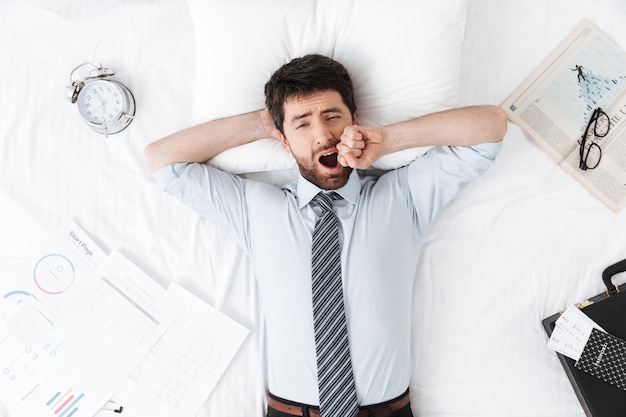 beau jeune homme d'affaires le matin au lit se trouve le bâillement