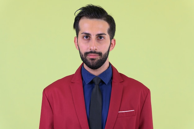 Beau jeune homme d'affaires persan barbu portant un costume contre un mur de couleur