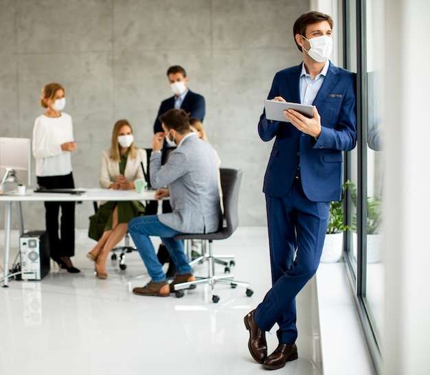 Beau jeune homme d'affaires portant un masque facial de protection tout en tenant une tablette numérique dans l'espace de bureau