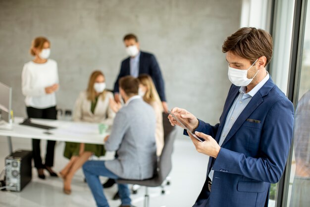 Beau jeune homme d'affaires portant un masque facial de protection tout en tenant une tablette numérique dans l'espace de bureau