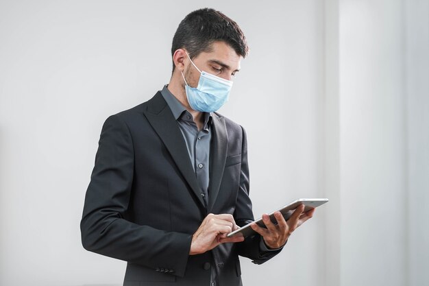 Beau jeune homme d'affaires portant un masque de protection travaillant avec une tablette sur fond blanc