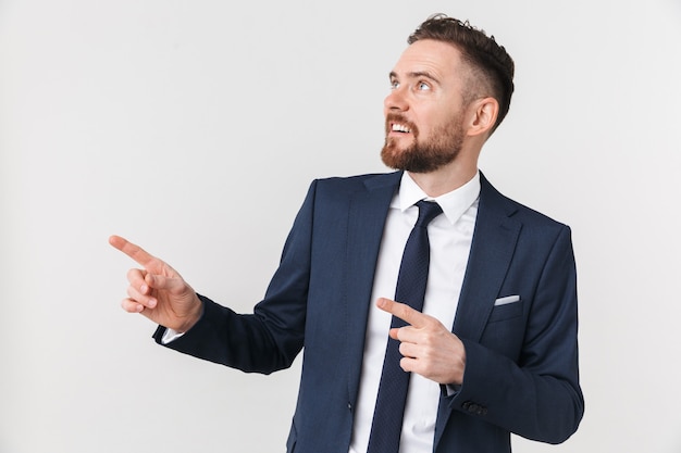 un beau jeune homme d'affaires posant isolé sur mur blanc pointant