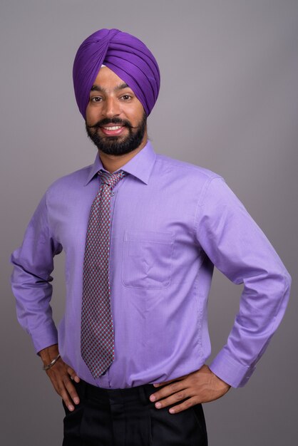Beau jeune homme d'affaires sikh indien portant turban sur gris