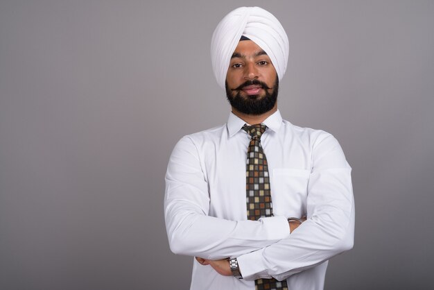 Beau jeune homme d'affaires sikh indien portant turban sur gris