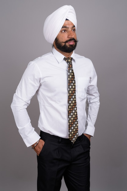 Beau jeune homme d'affaires sikh indien portant turban sur gris